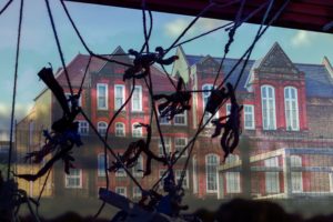 Several hand made puppets are hung in front of a window.