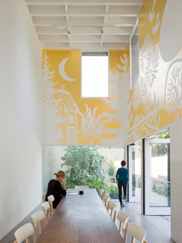 People in a bright cafe space. There is a long wooden table and lots of windows.