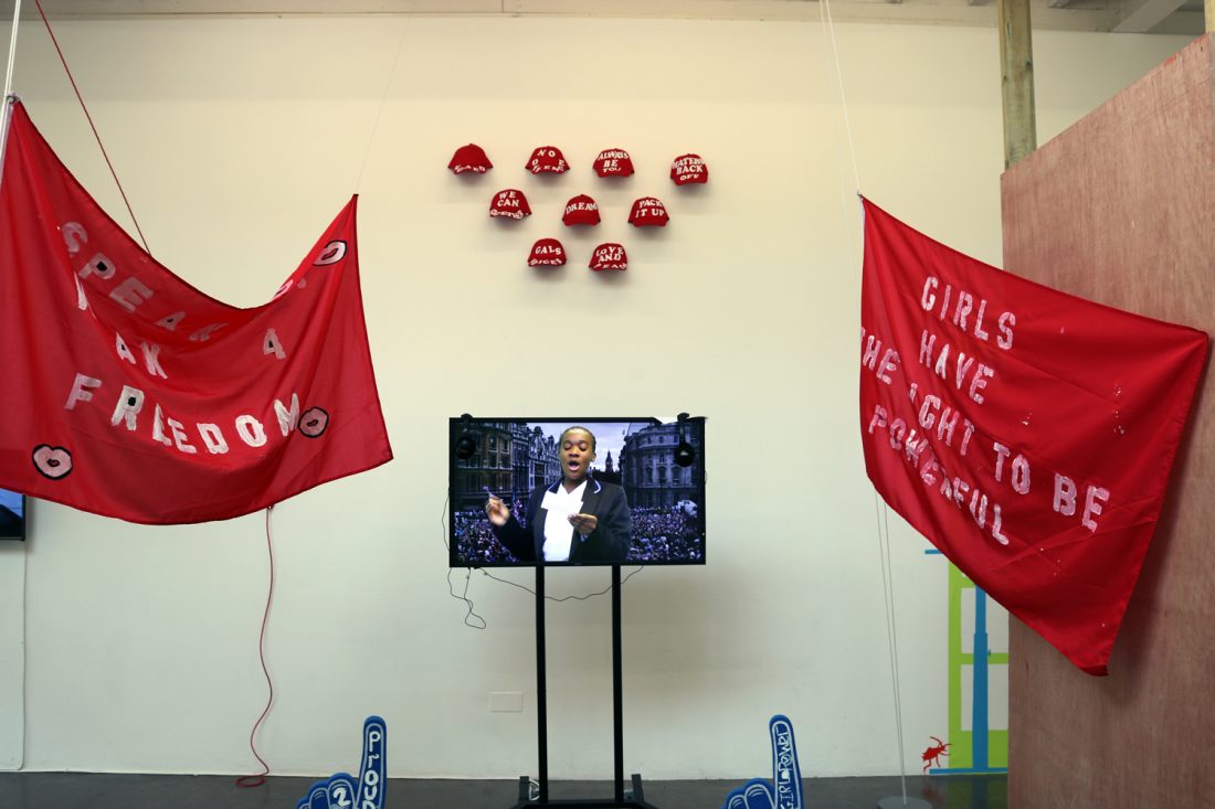 <p>Campaign video flanked by two red flags bearing slogans about women’s and girls’ rights as part of The Schools’ Exhibition: Jack Petchey Start Programme in the Clore Studio, 2017</p>