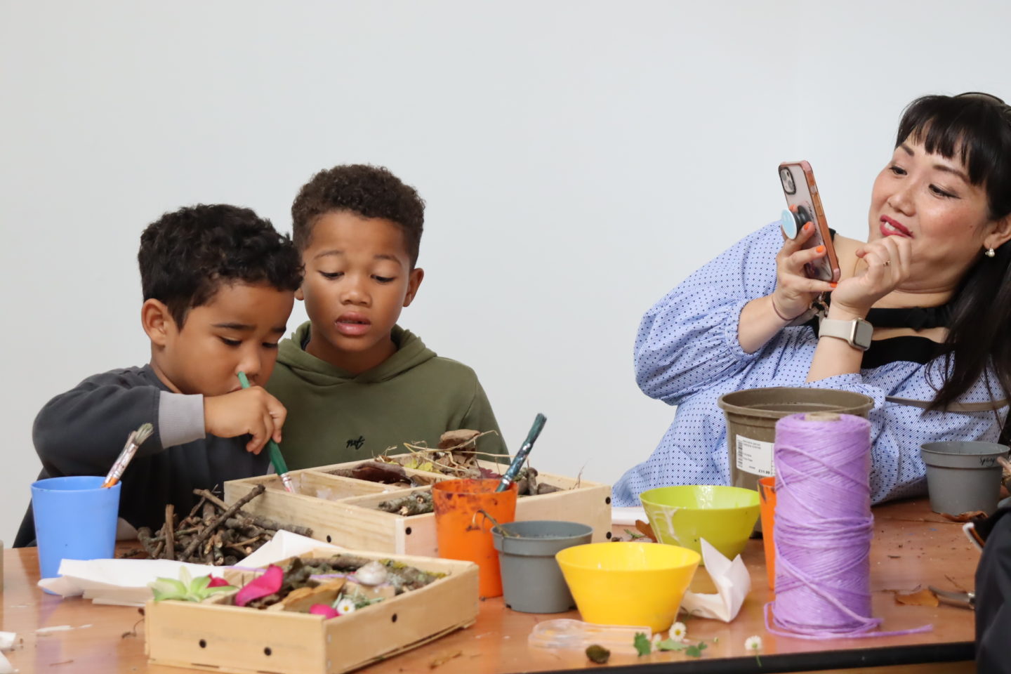 Two young boys make a bug hotel together. An adult beside them is smiling and taking a photo of them.