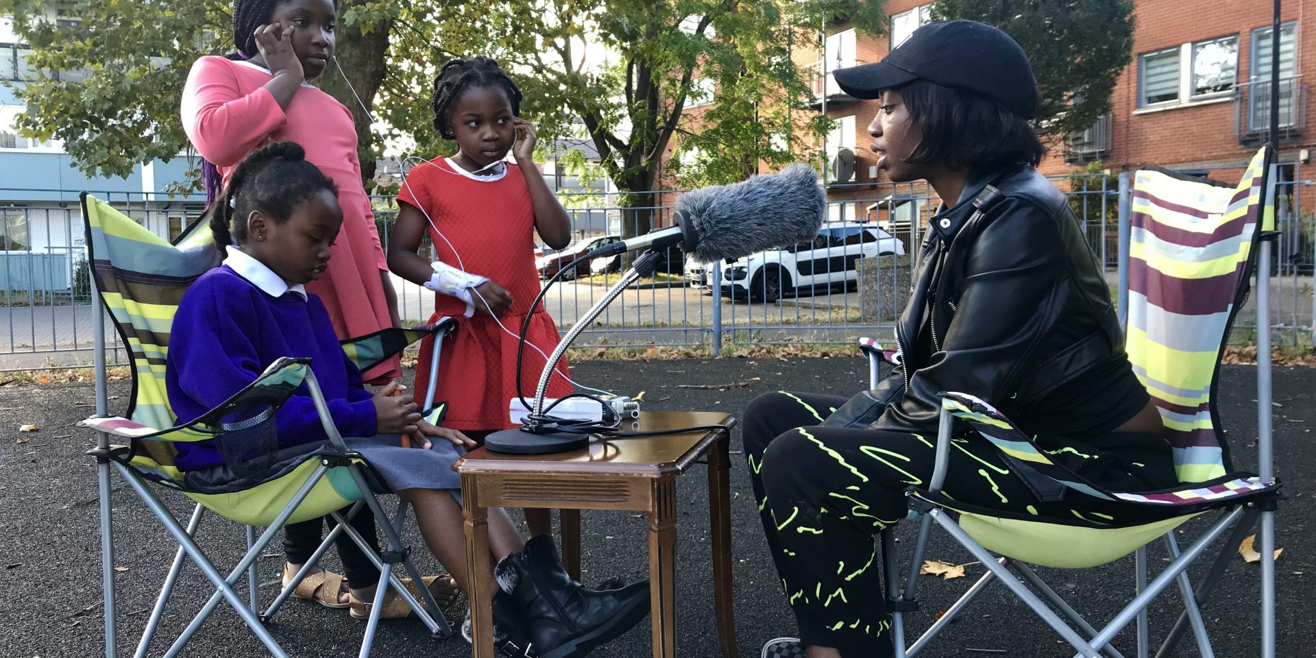 Three children interview an adult sat outside