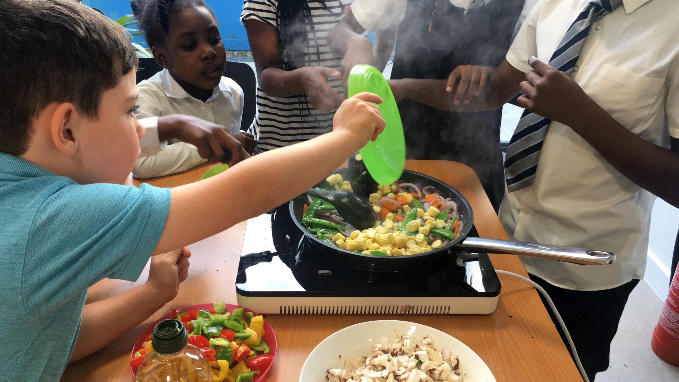 Children put vegetables into a frying pan to cook stir fry