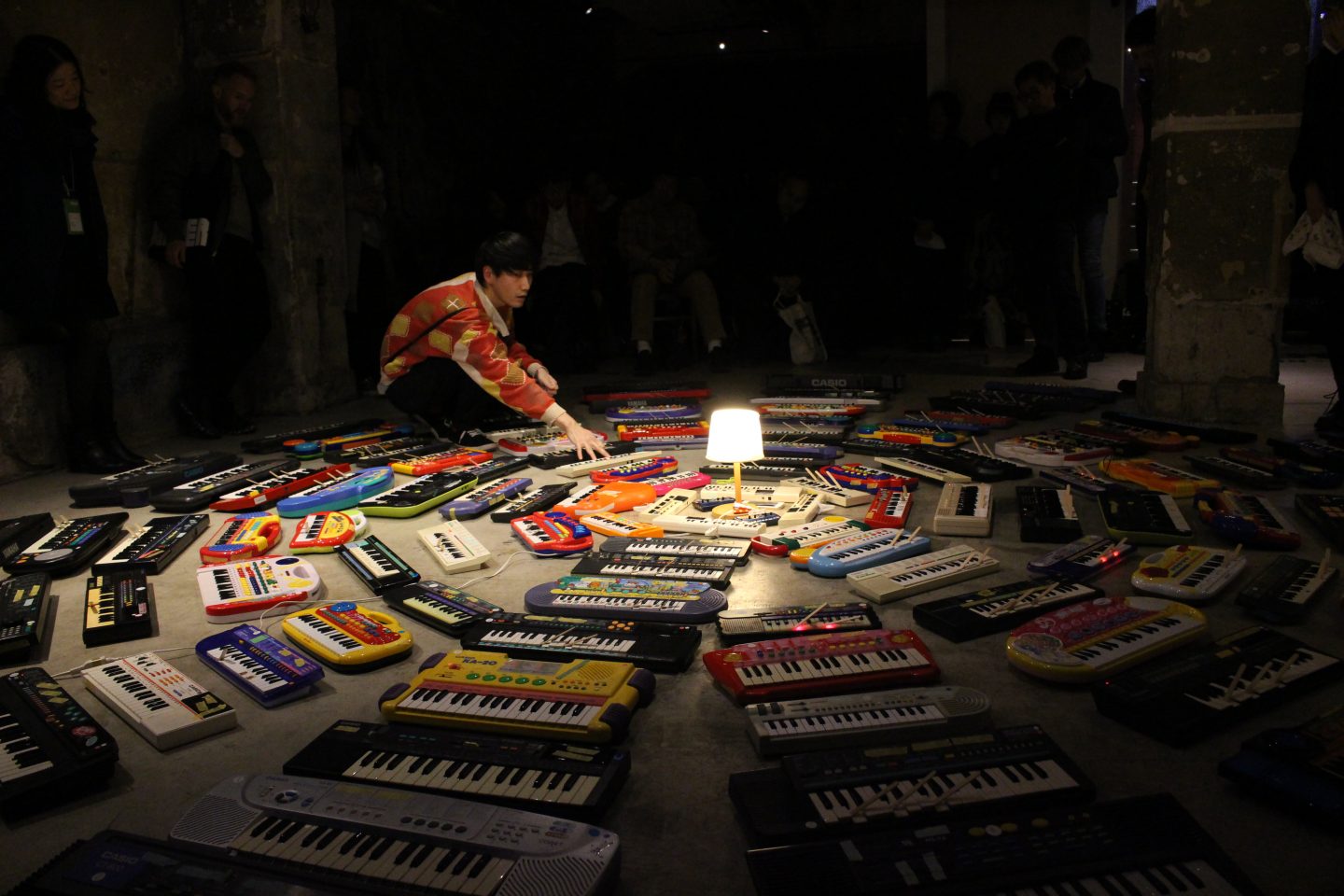 The artist sits at the edge of concentric circle of keyboards placed on the floor