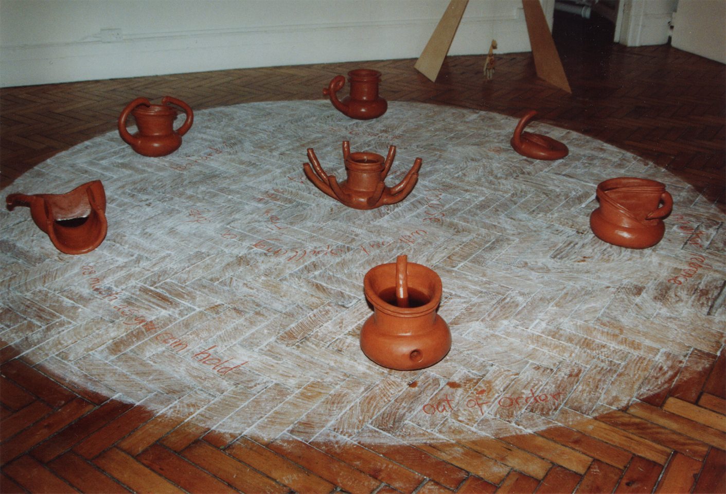 A parquet floor with a white circle drawn on, with terracotta objects positioned in the circle