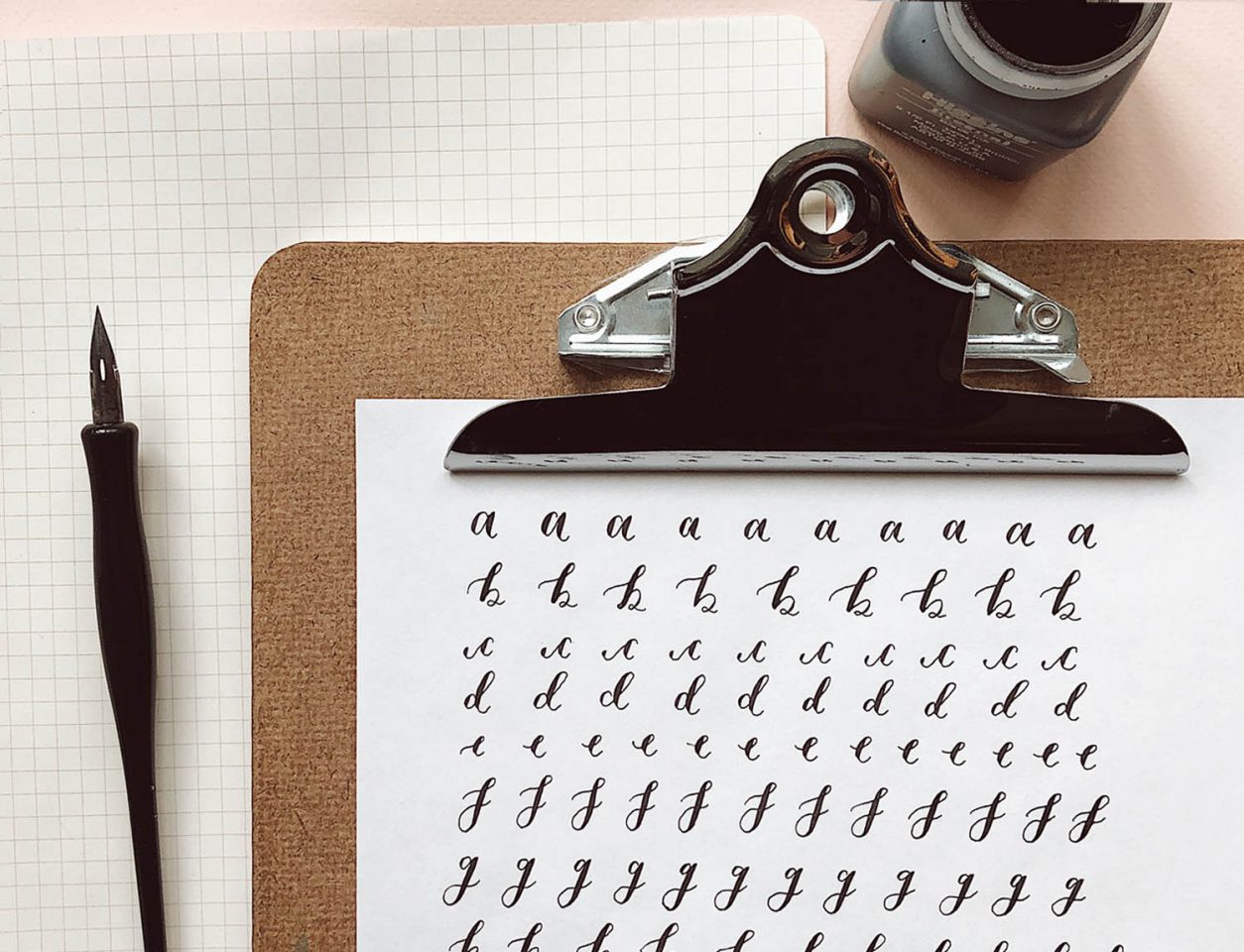 A clipboard with a hand-alphabet on paper written in ink