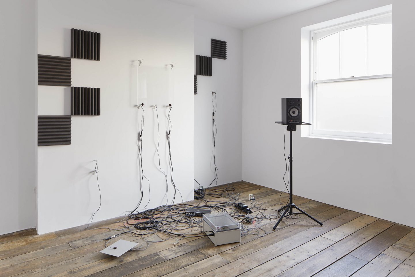 A tangle of wires on the floor linked to a free standing speaker and speakers wall mounted