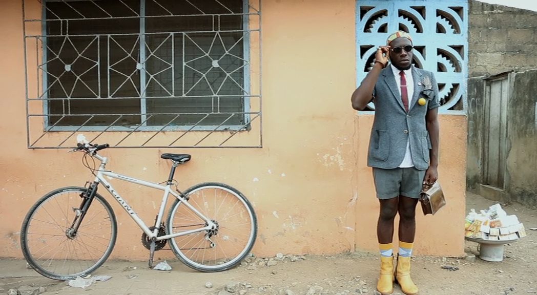 A person wearing a suit and sunglasses standing outside a building as though waiting