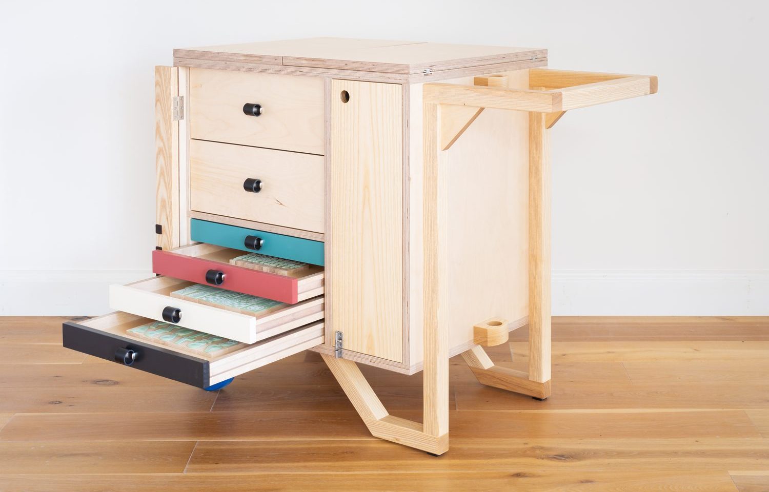 A wooden set of drawers mounted on two wheels. The draws are open revealing wooden blocks used for printing letters
