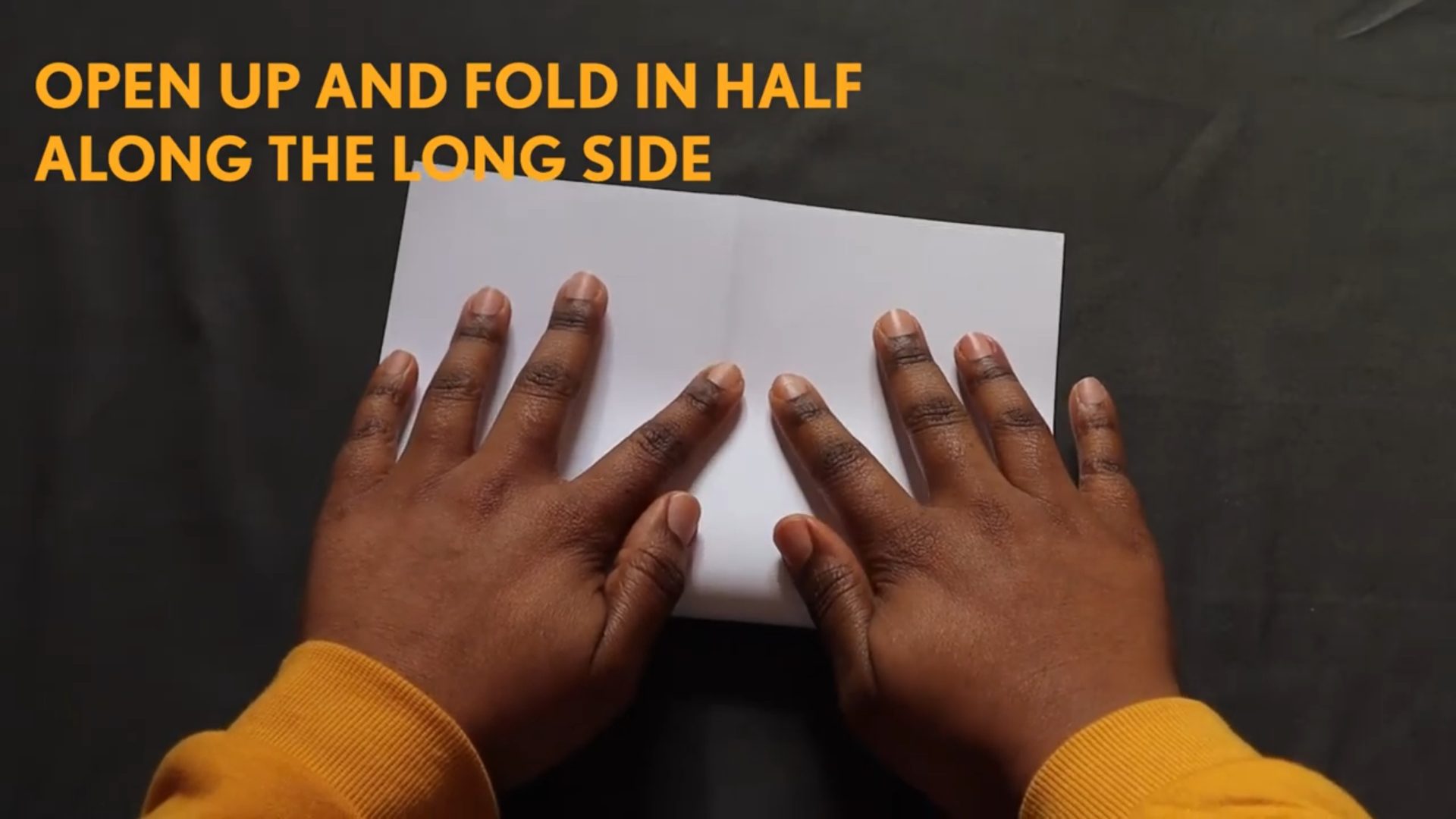 Hands folding a zine with a written instruction: Open up and fold in half along the side