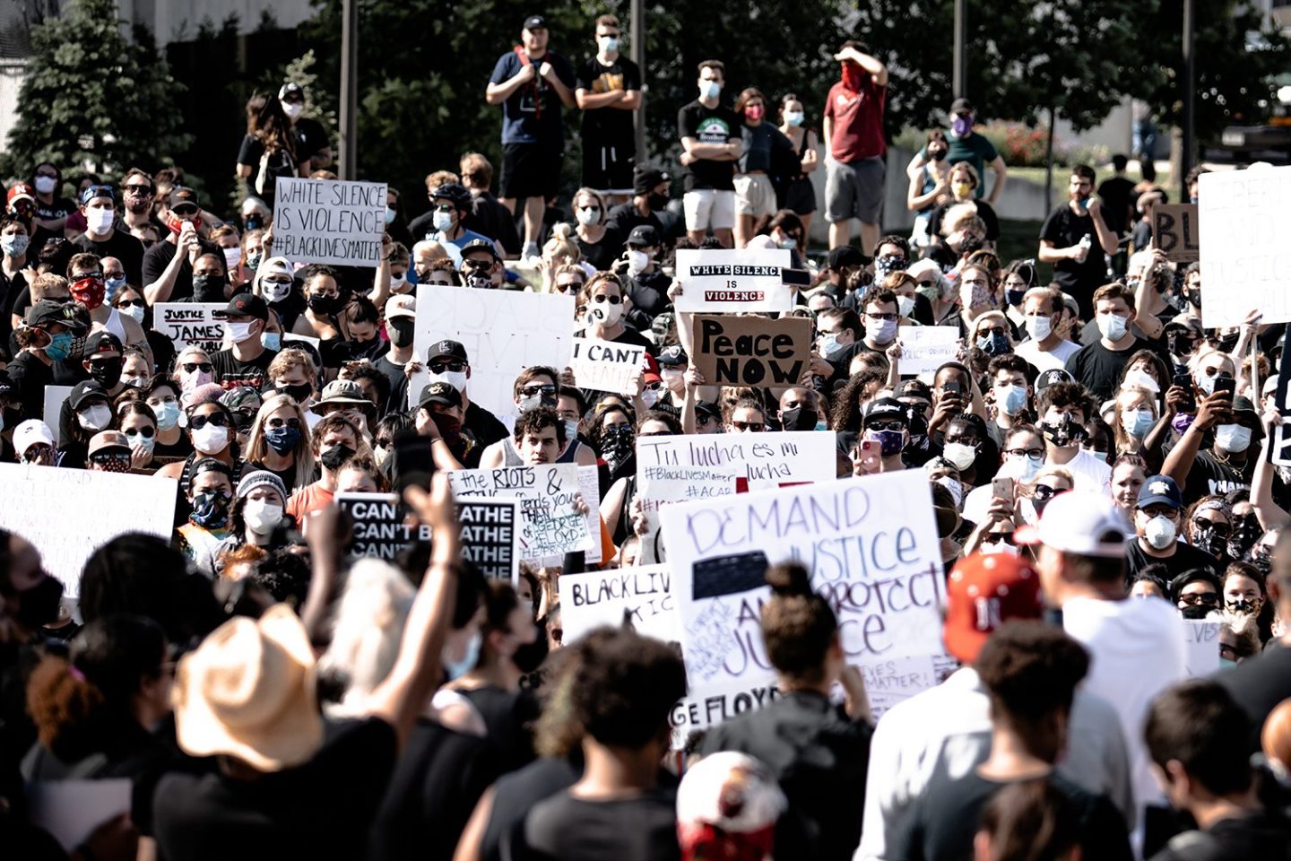 A crowd of protesters wearing masks and holding placards protest against police brutality and racism in the US