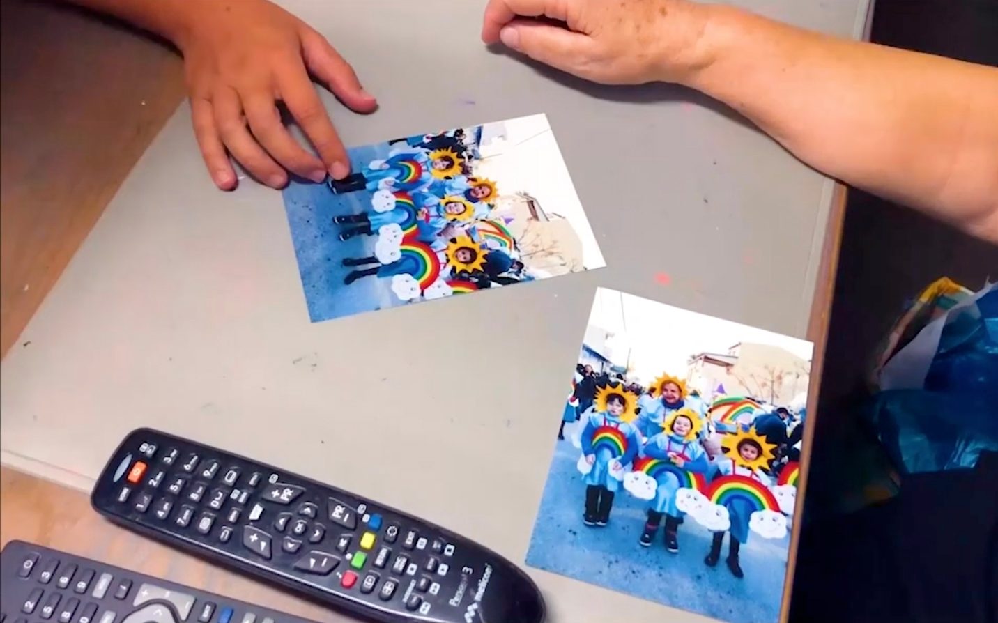 Two photographs of children wearing flower costumes on a table, next two TV remotes