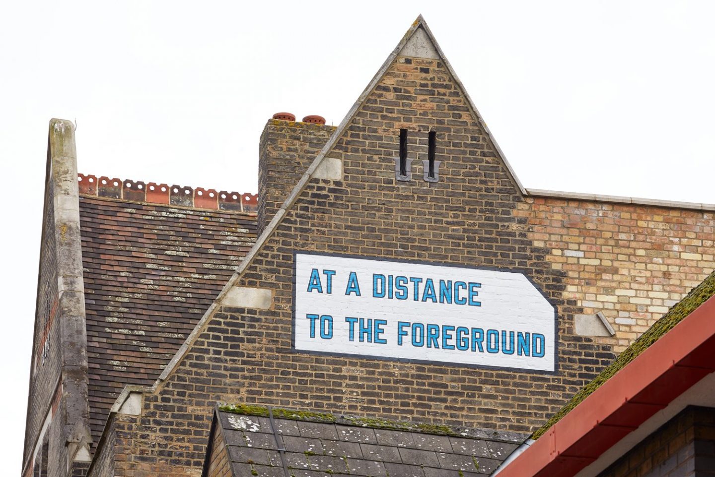 AT A DISTANCE TO THE FOREGROUND in a rectangular white box, lined in blue, painted onto the side of the Fire Station