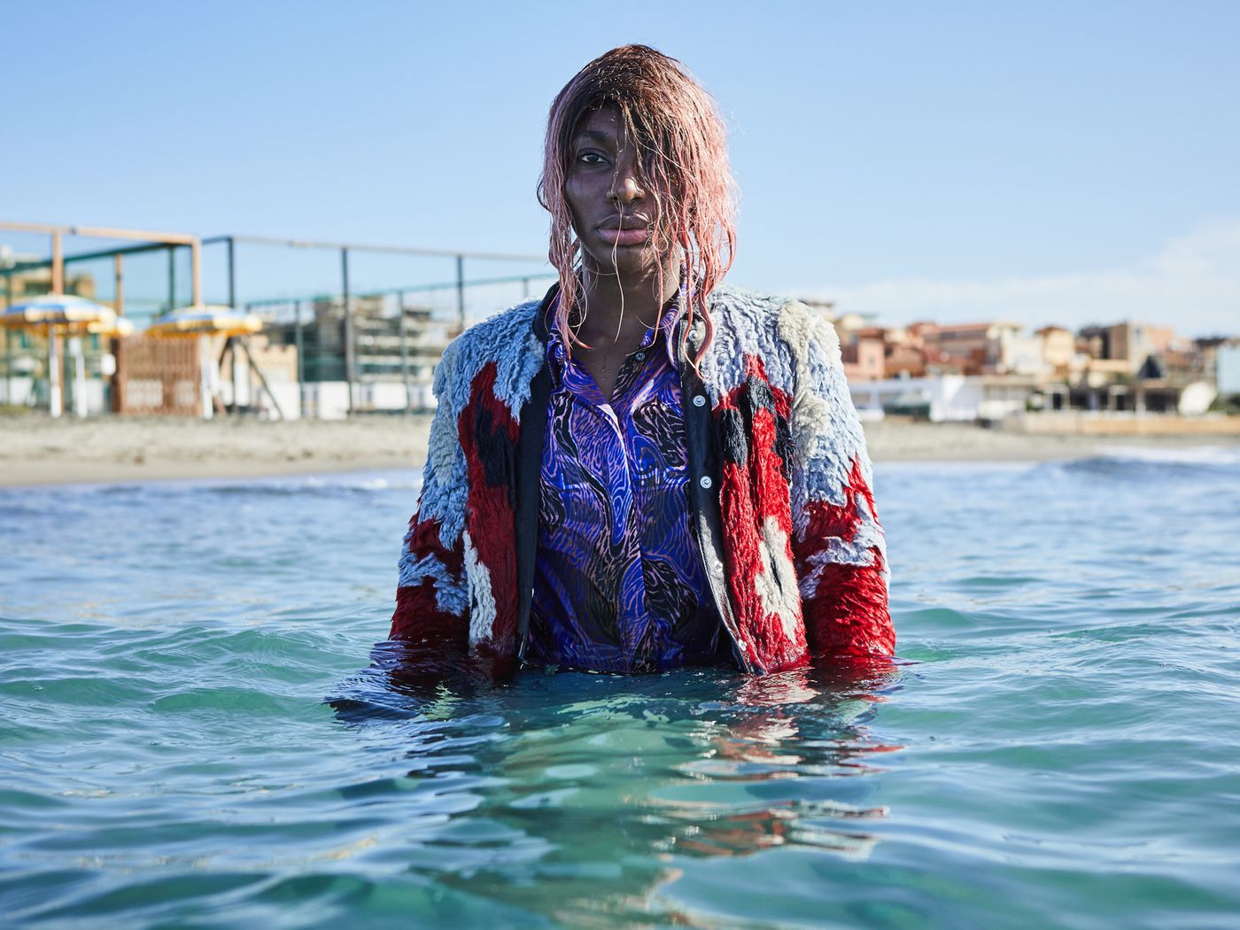 Michaela Coel stands in the sea with pink hair