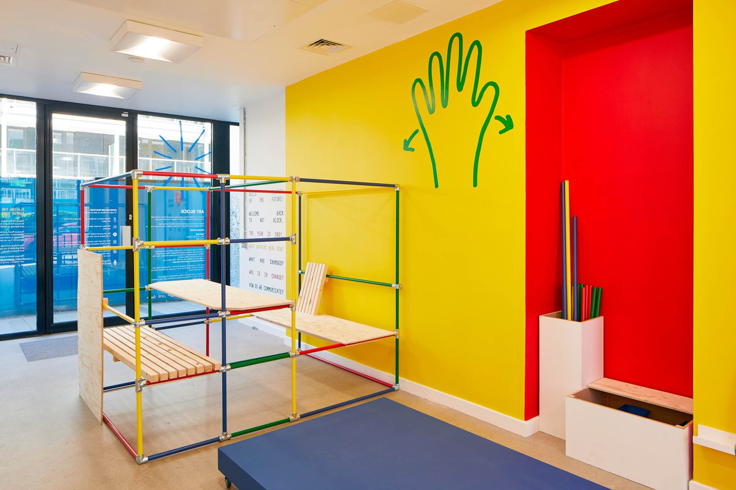 Art Block with a brightly coloured yellow wall, a brightly coloured wood modular structure and a green hand painted onto the wall