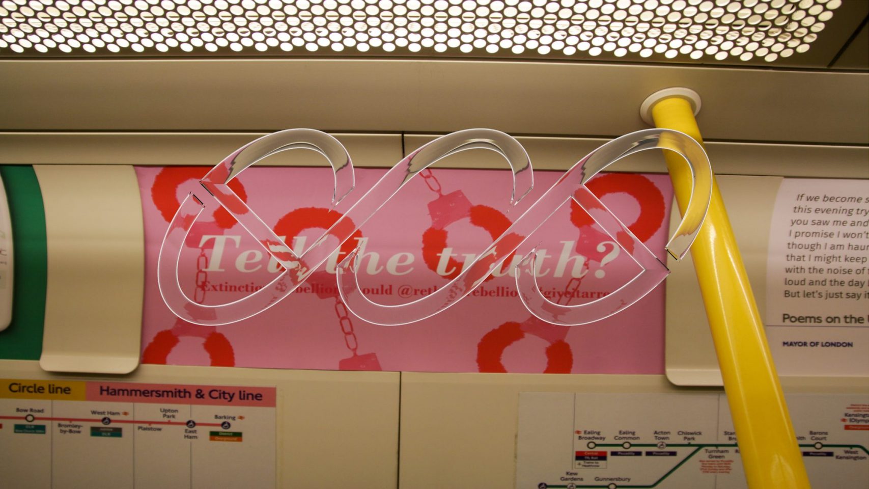 A photo of an landscape-orientated advertisement panel inside a London underground tube service. The advert is pink with red chains in teh background, a white text reads 'Tell the Truth?'