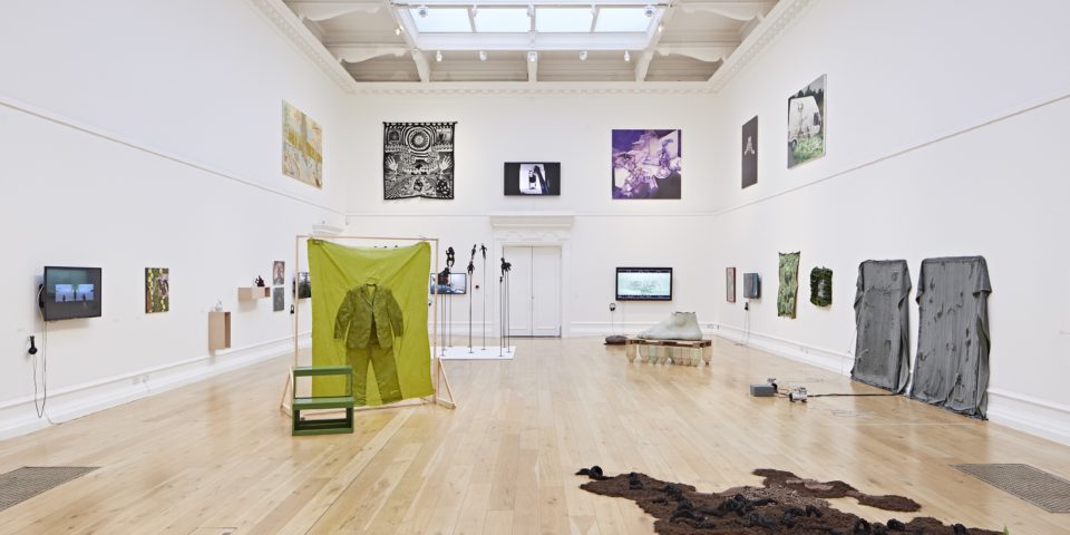 A photo of a large gallery space with many art installations around the room and the walls.