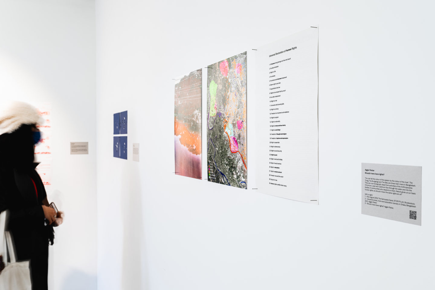 Image of a bright gallery space with a person looking at several art works installed onto the gallery wall.