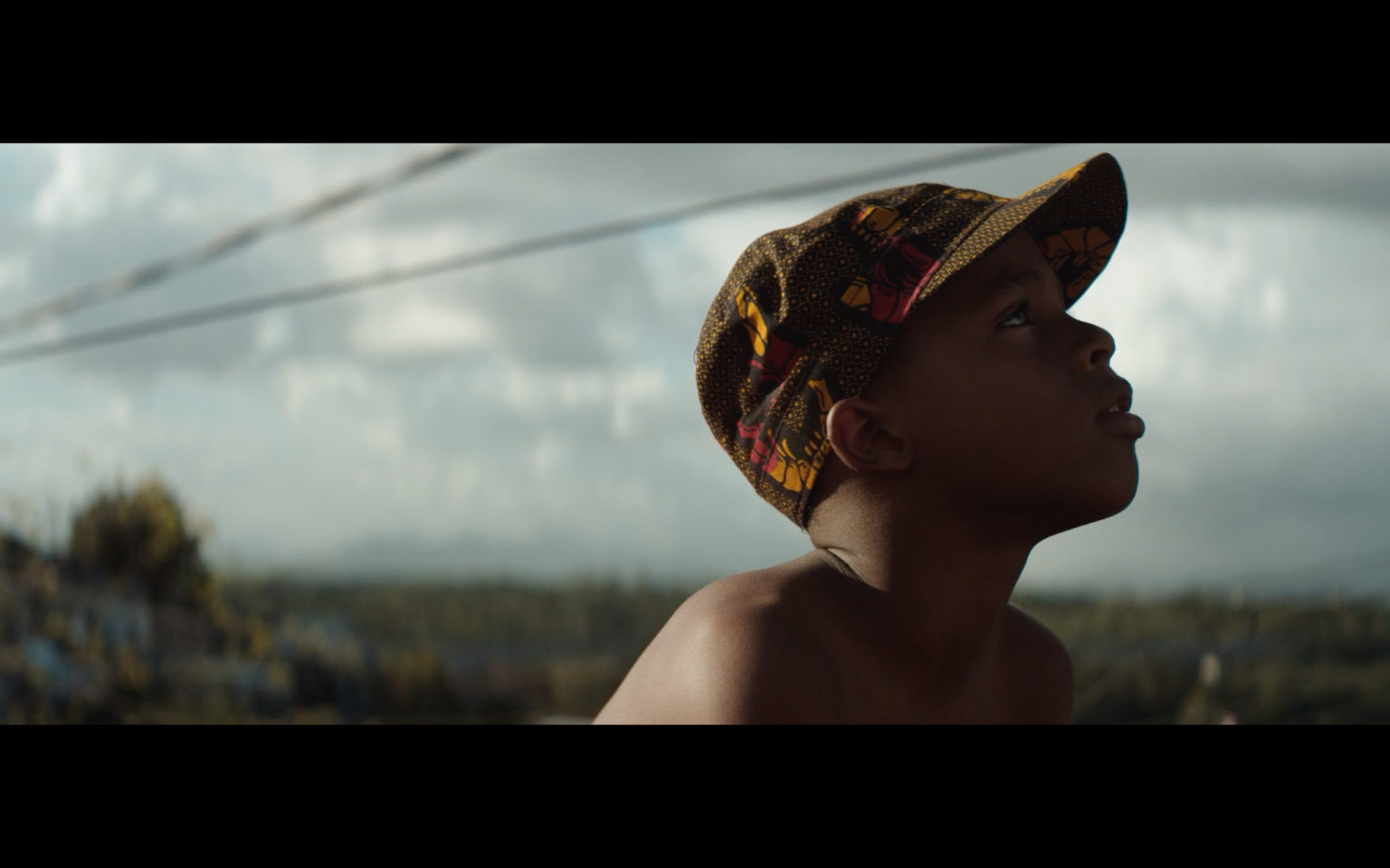 A boy wearing a hat looks up towards a grey sky