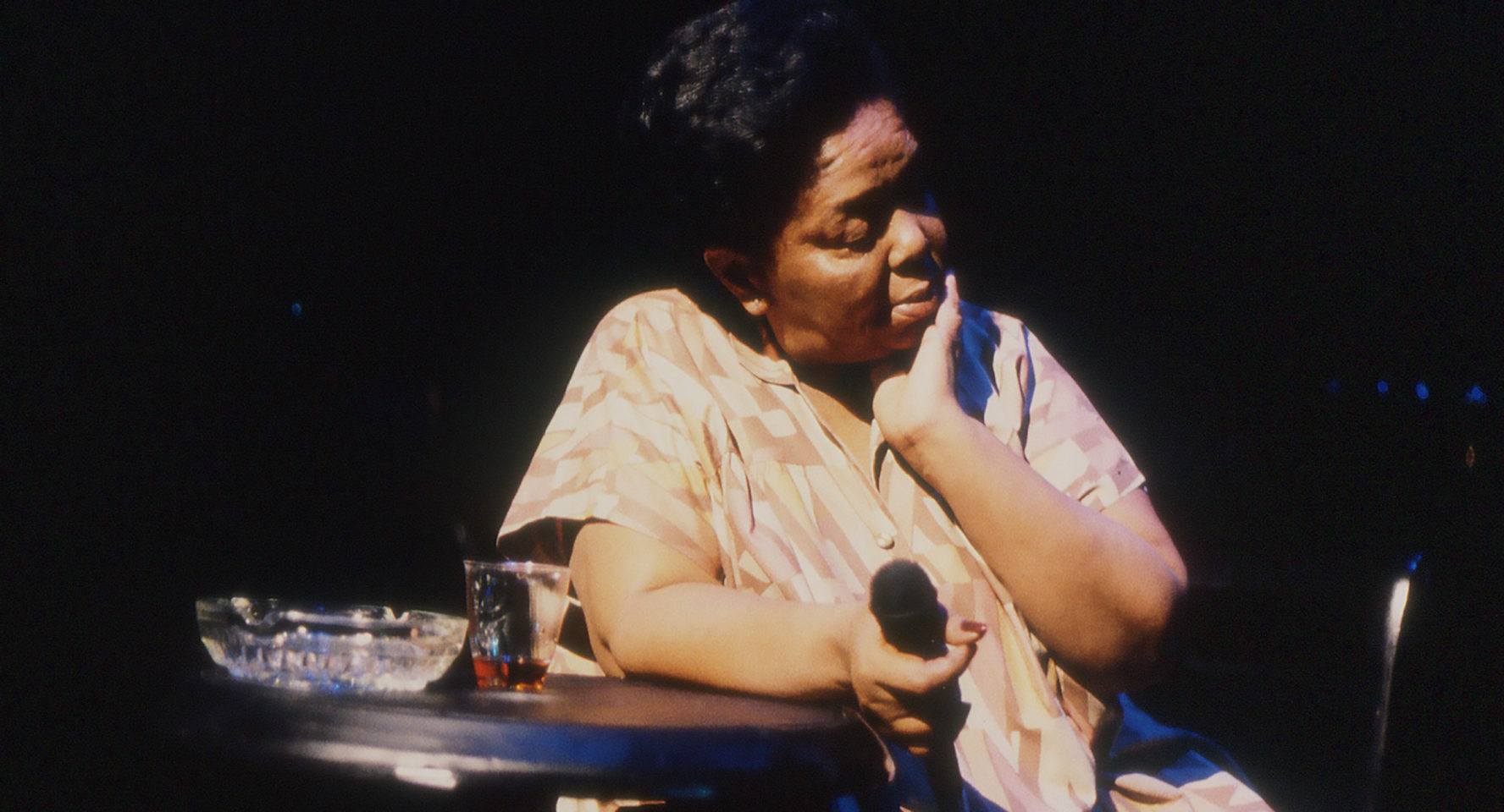 A woman sitting down holds a microphone and looks off to her left.