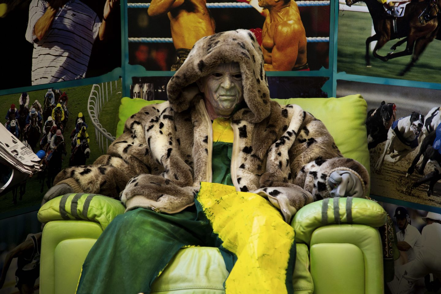 A man in a mask sits on a chair surrounded by photographs