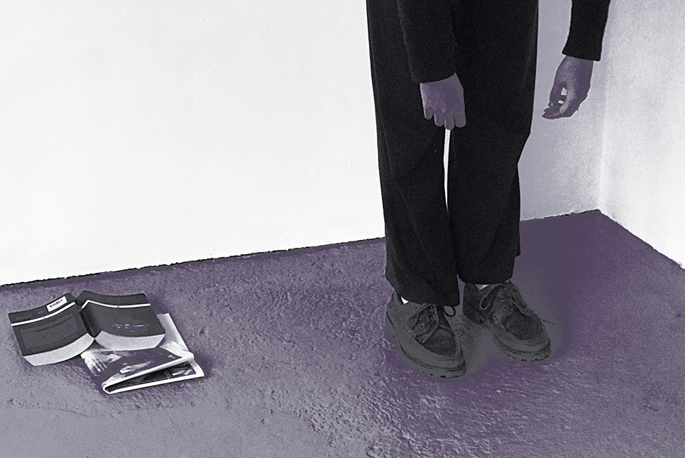 A high contrast monochrome image of the bottom half of a person leaning forwards, to the left there is a newspaper and a book on the floor