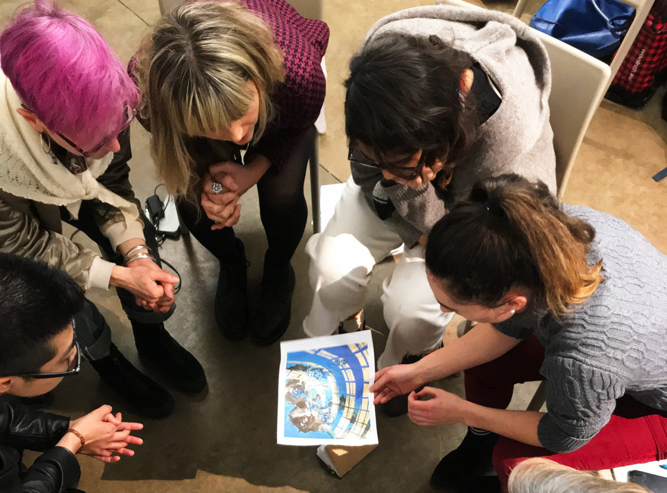 A group of people sitting in a circle examining an artwork on a piece of paper