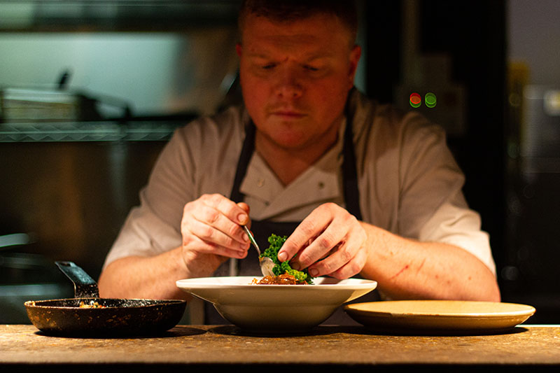 A chef in a restaurant kitchen putting the finishing touches on a plate of food