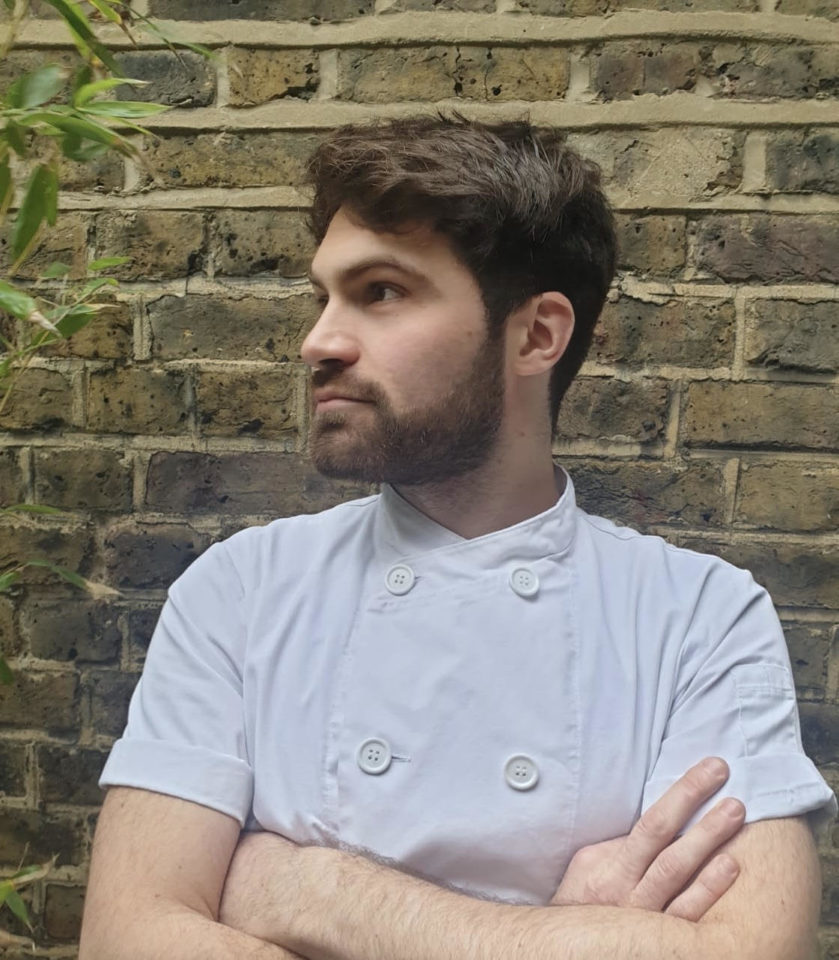 A chef stands with his arms crossed looking away from the camera