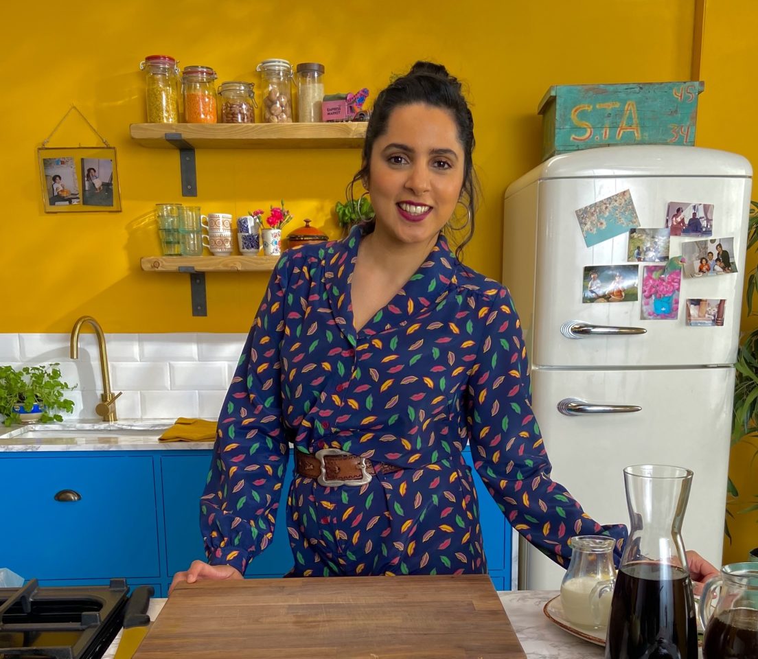 A woman wearing a blue dress stands in a bright yellow kitchen