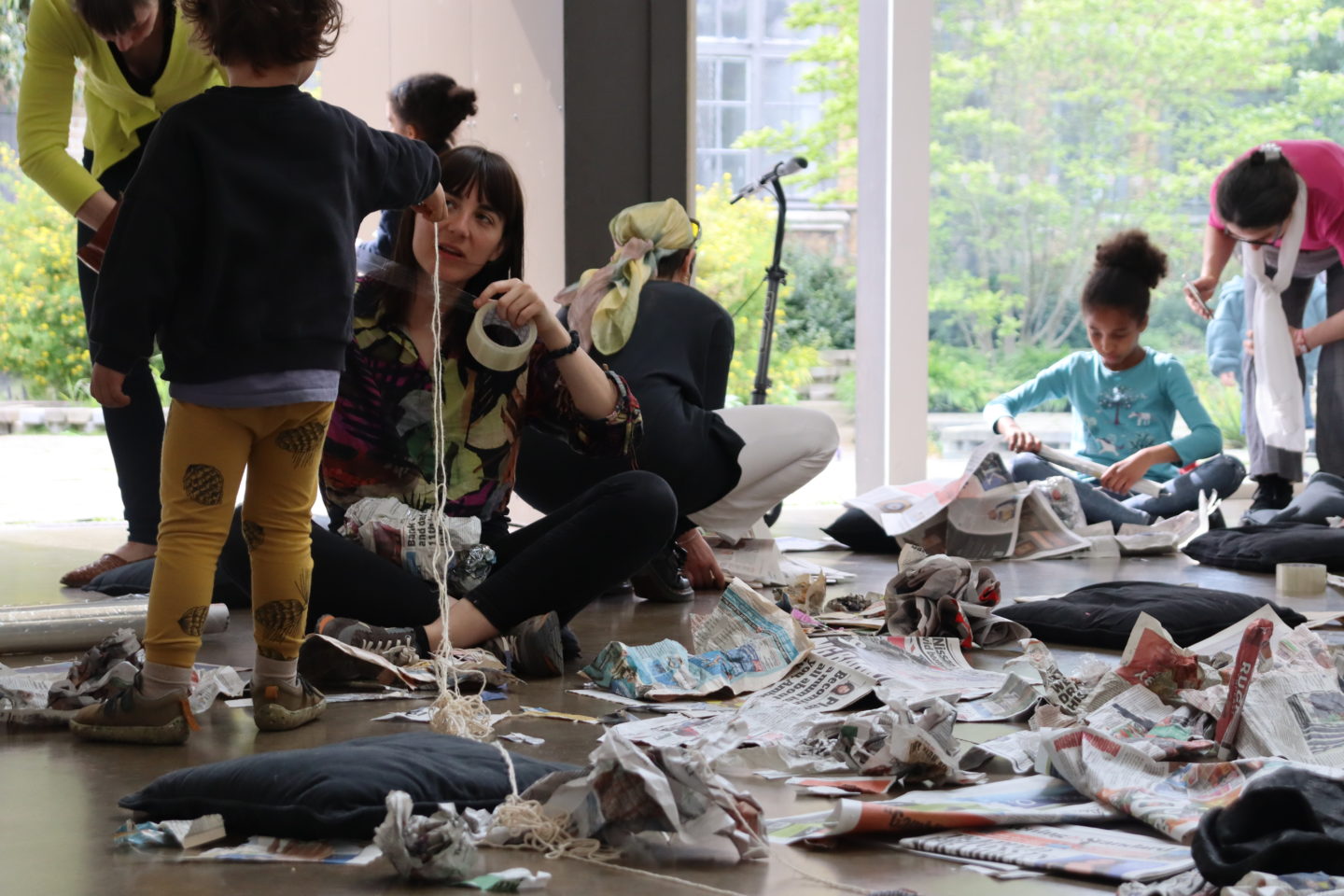 Children making newspaper sculptures in a room with large windows and newspaper scattered on the floor
