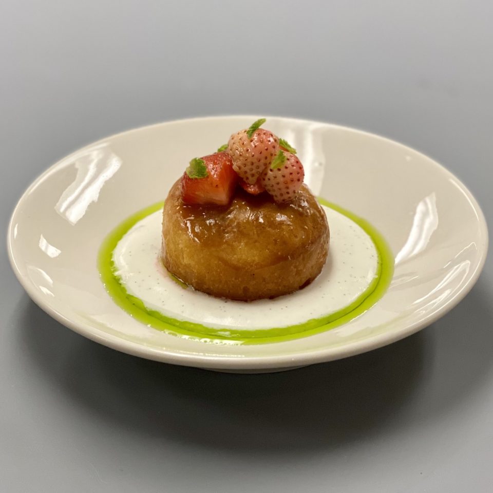 A bowl with a dessert in it. The dessert has strawberries on top. The bowl is sat on a grey table