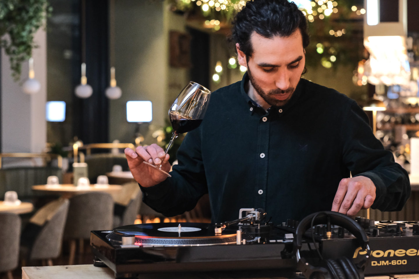 A man holding a glass of red wine plays a record on a turntable