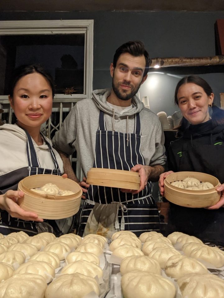 Three chefs stand in front of a table. The table is covered in Bao buns.