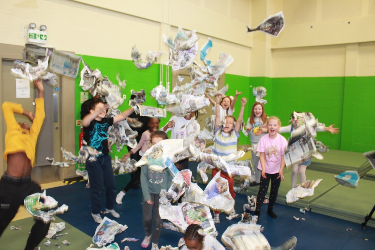 Children in a creative workshop throw newspapers in the air.