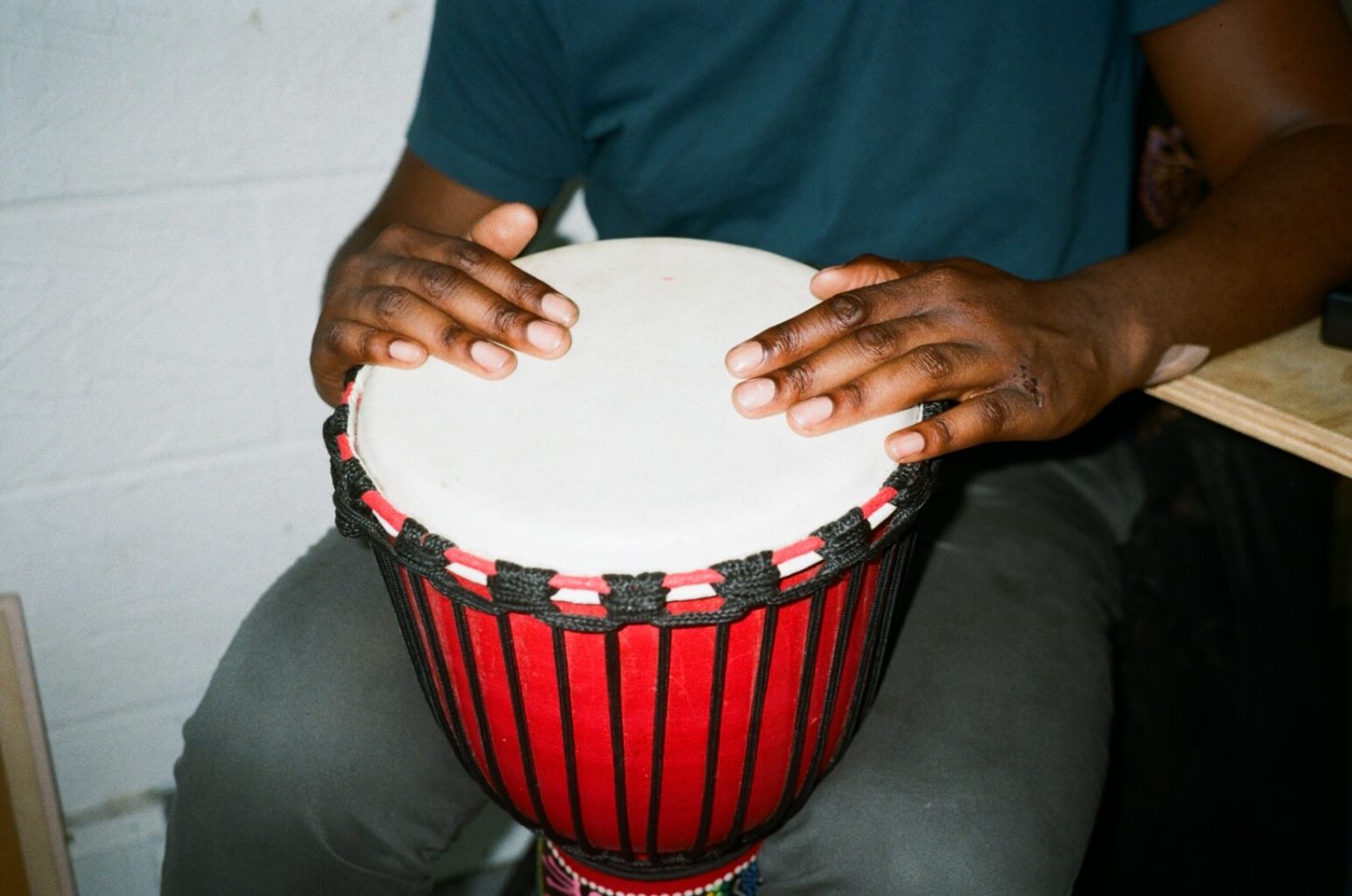A person holds a drum between their legs and are playing it with their hands.