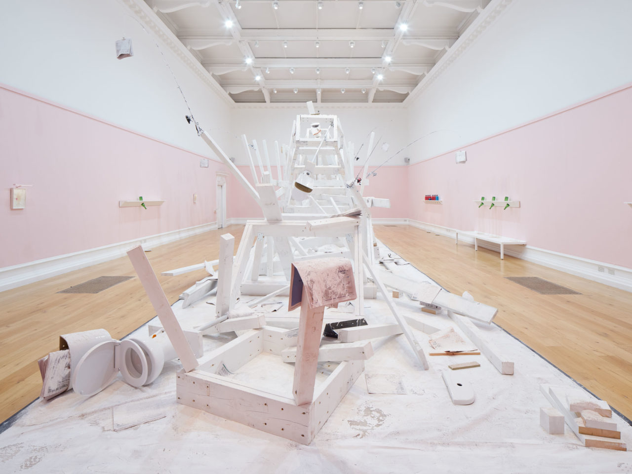 A wooden installation painted white and covered in flour in the centre of a large gallery with pink and white walls.
