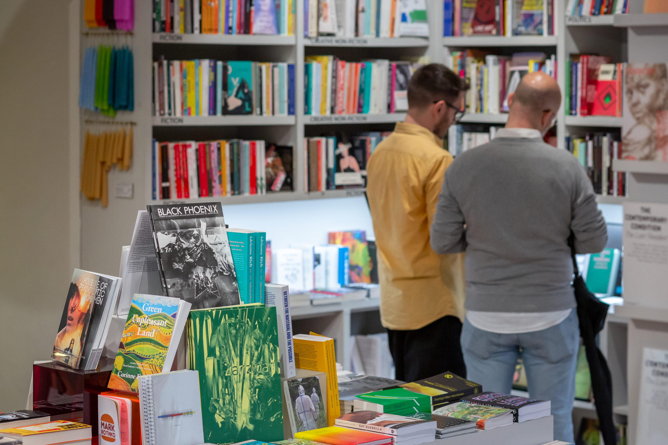 Two men stand in a book shop looking at books.