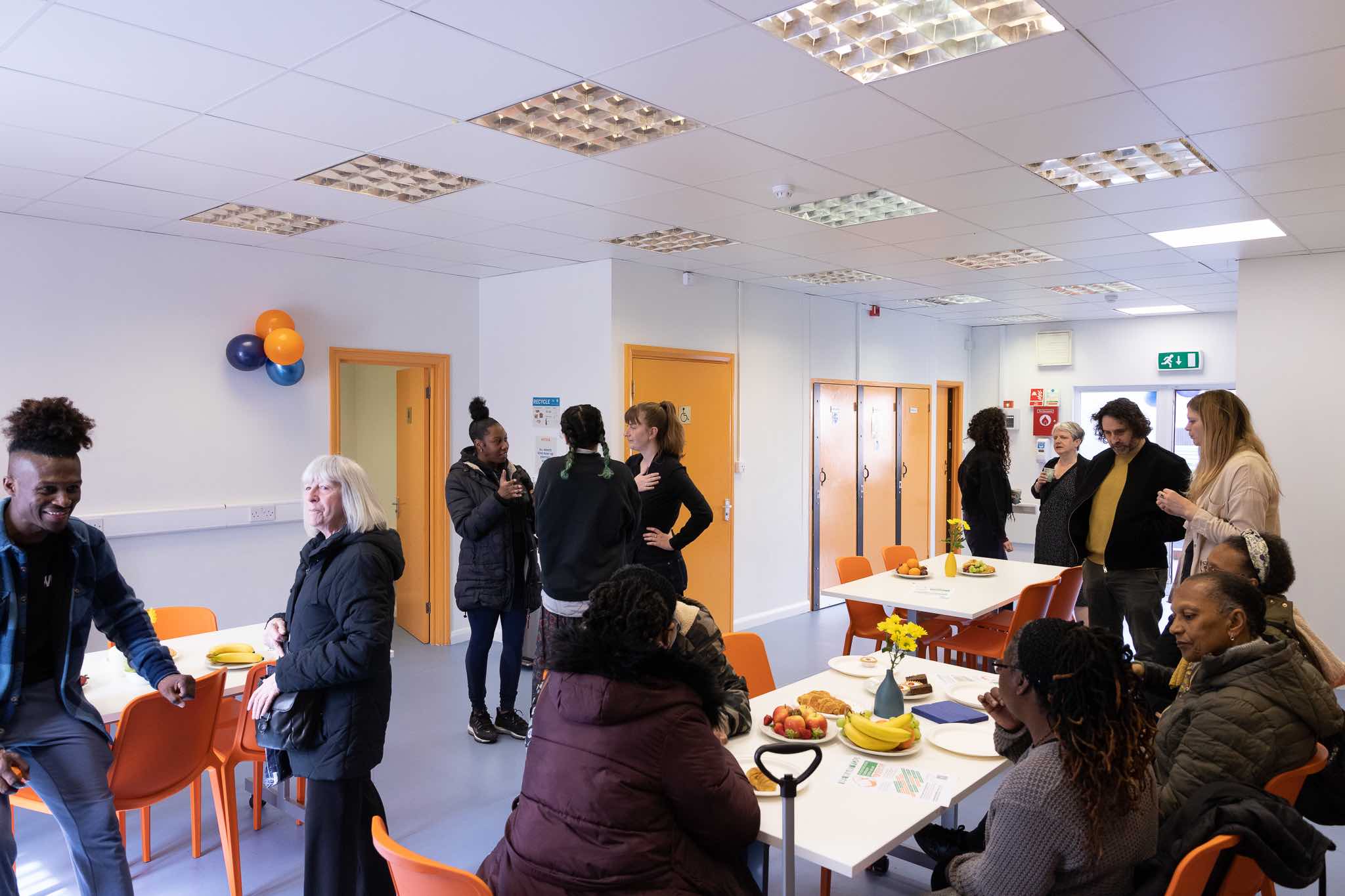 People gather in a bright community hall. They are all speaking in different groups.