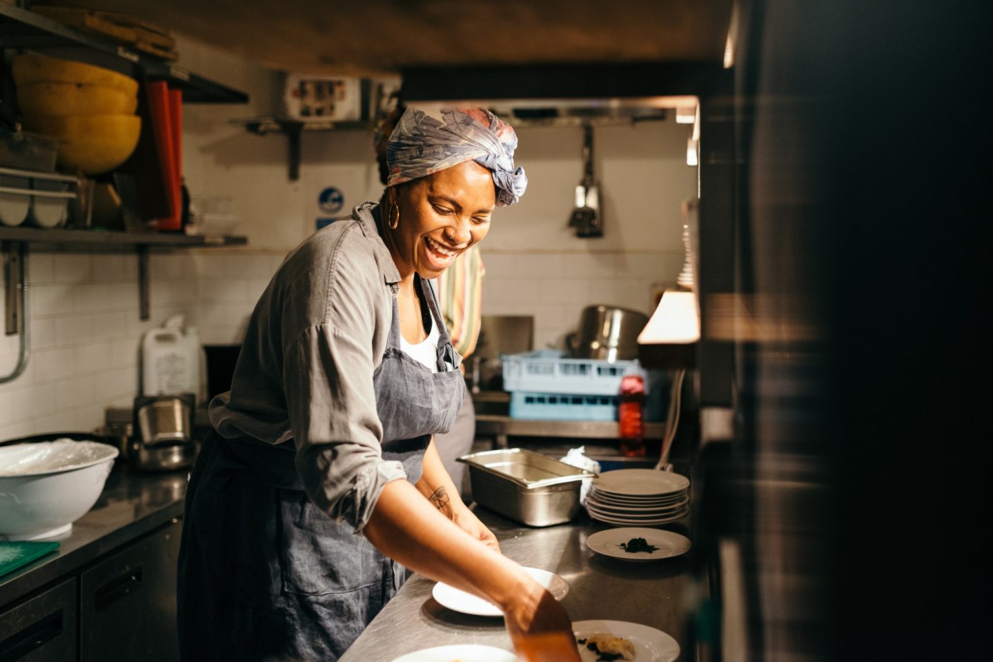 A woman smiling in a kitchen as she prepares food.