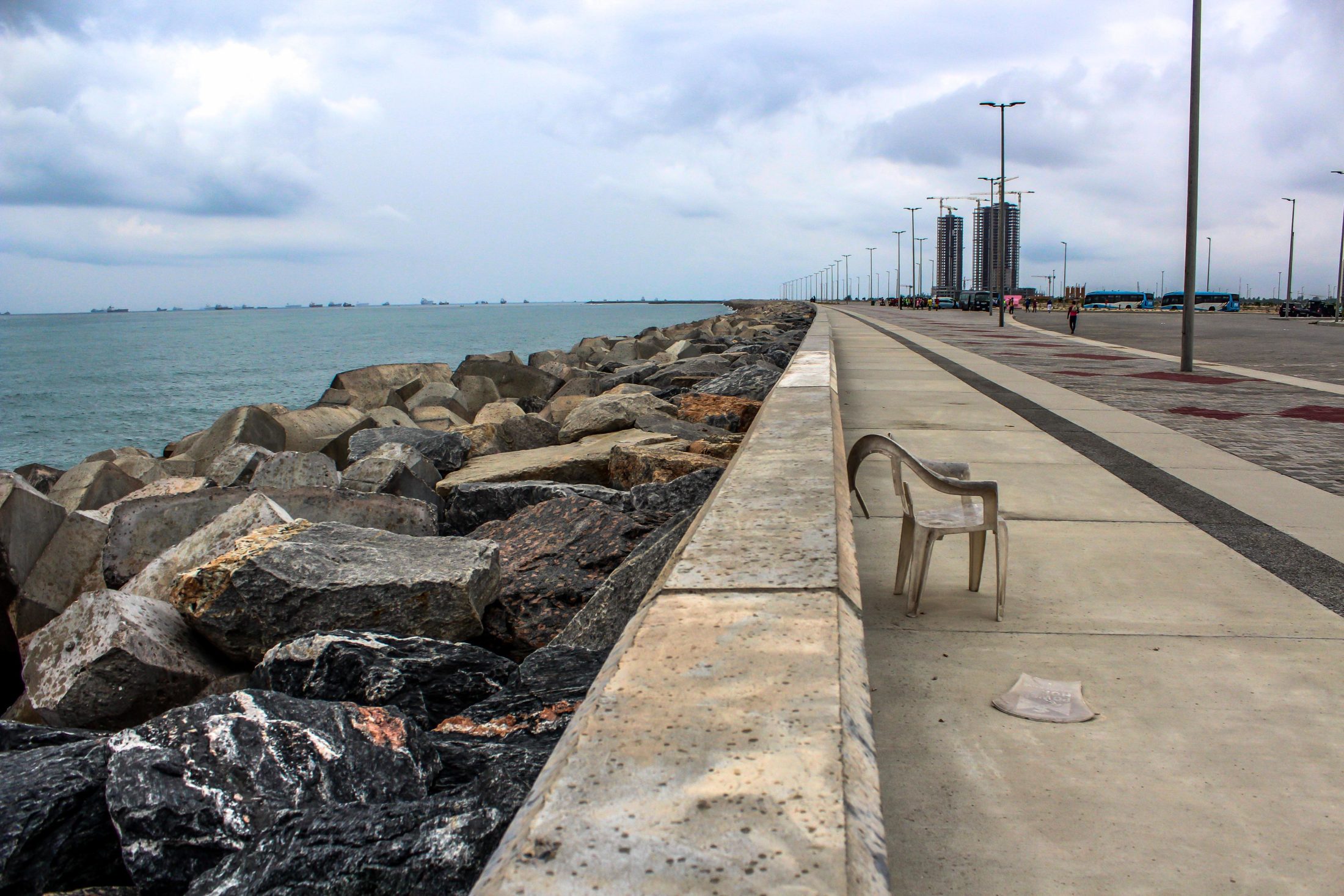 A broken plastic chair on a long concrete road beside the sea.