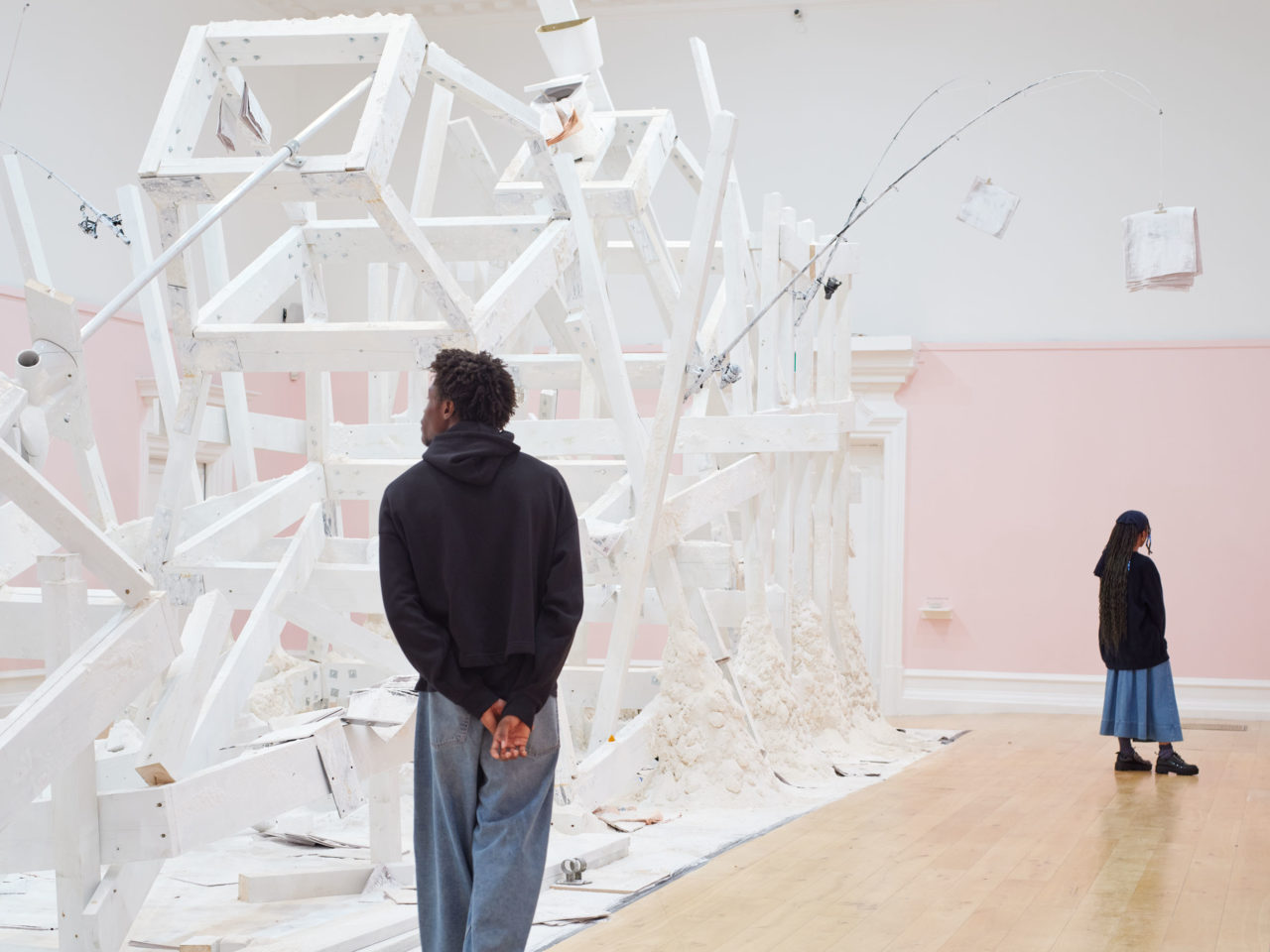 A wooden installation by artist Pope.L painted white and covered in flour in the centre of a large gallery with pink and white walls.