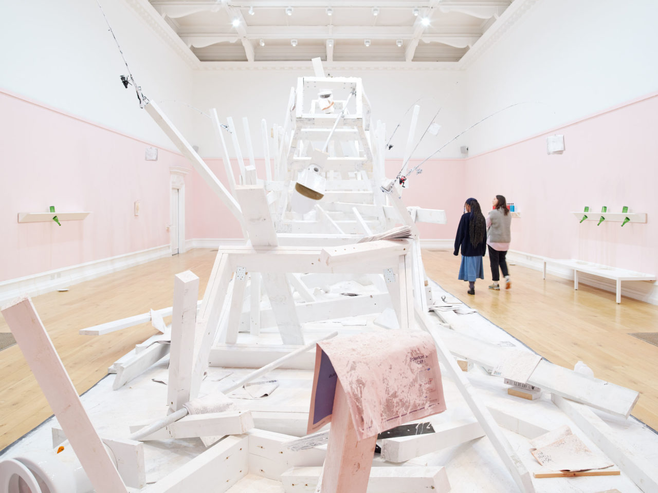 A wooden installation by artist Pope.L painted white and covered in flour in the centre of a large gallery with pink and white walls.