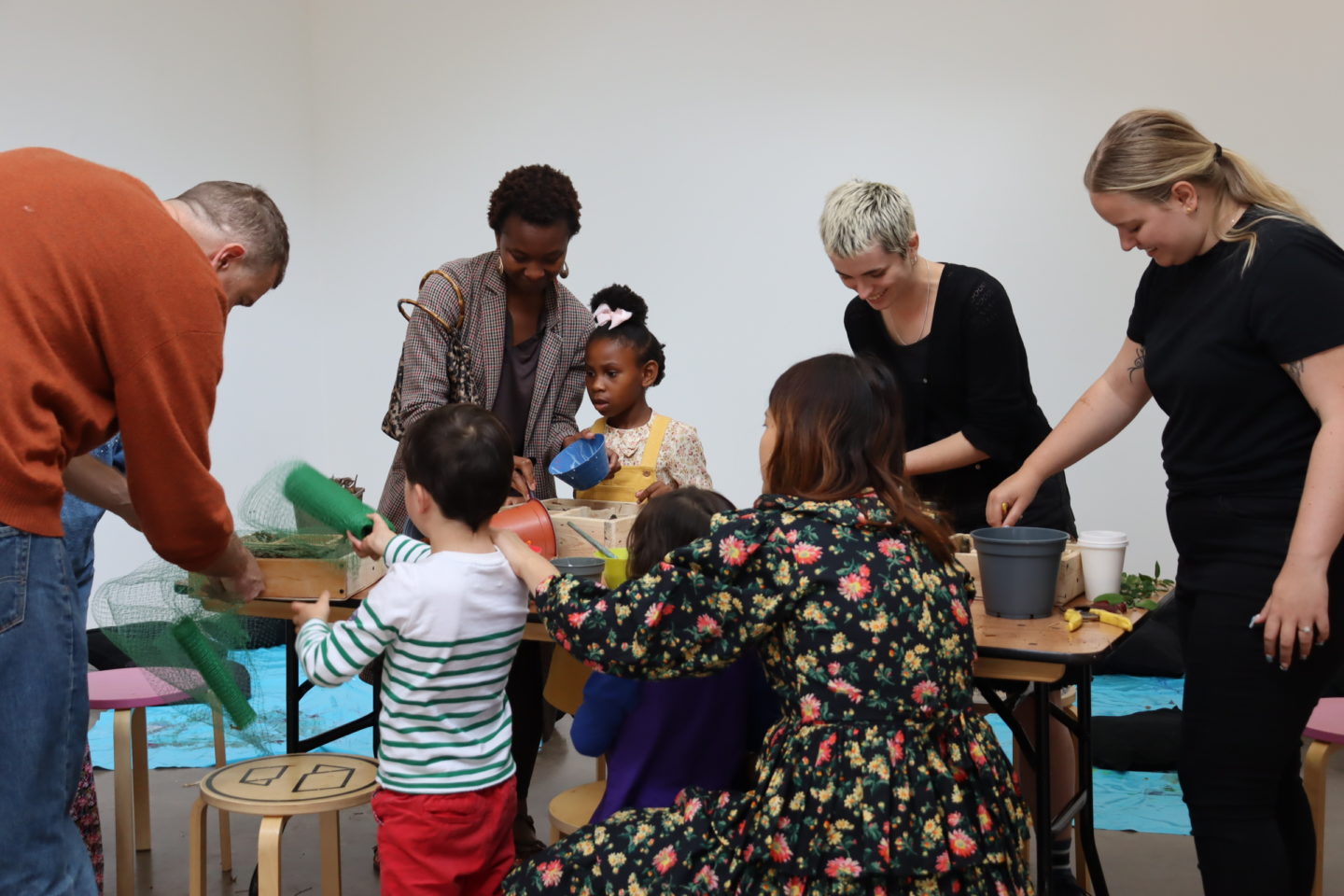 Young people and adults do arts and crafts together around a table in a white room.