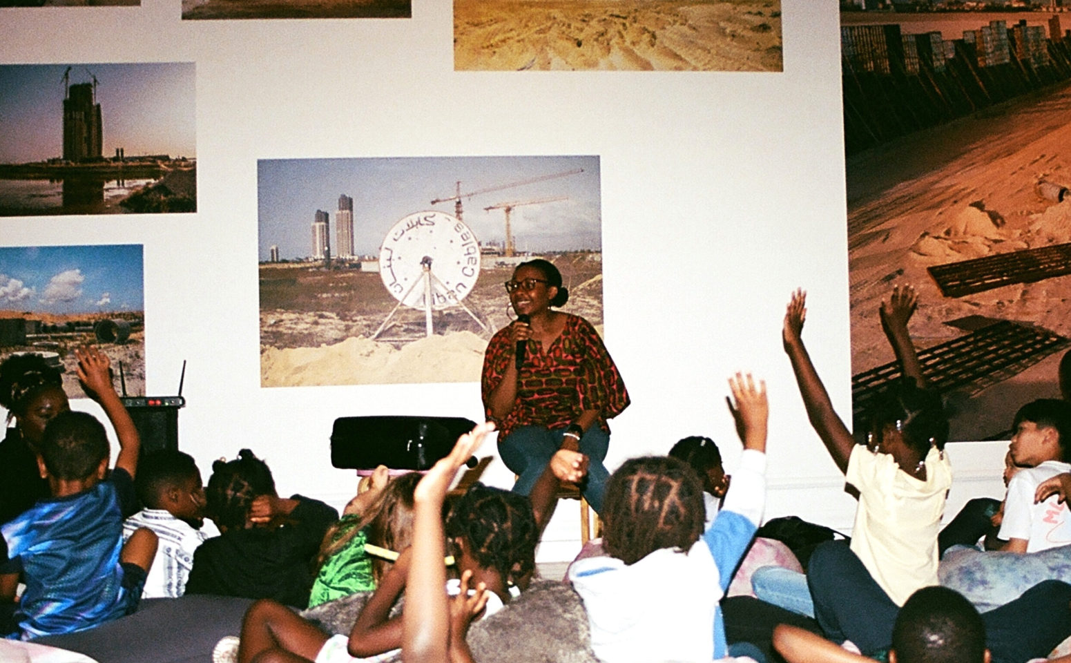 A group of children sitting on the ground in an art gallery listening to an adult tell stories.