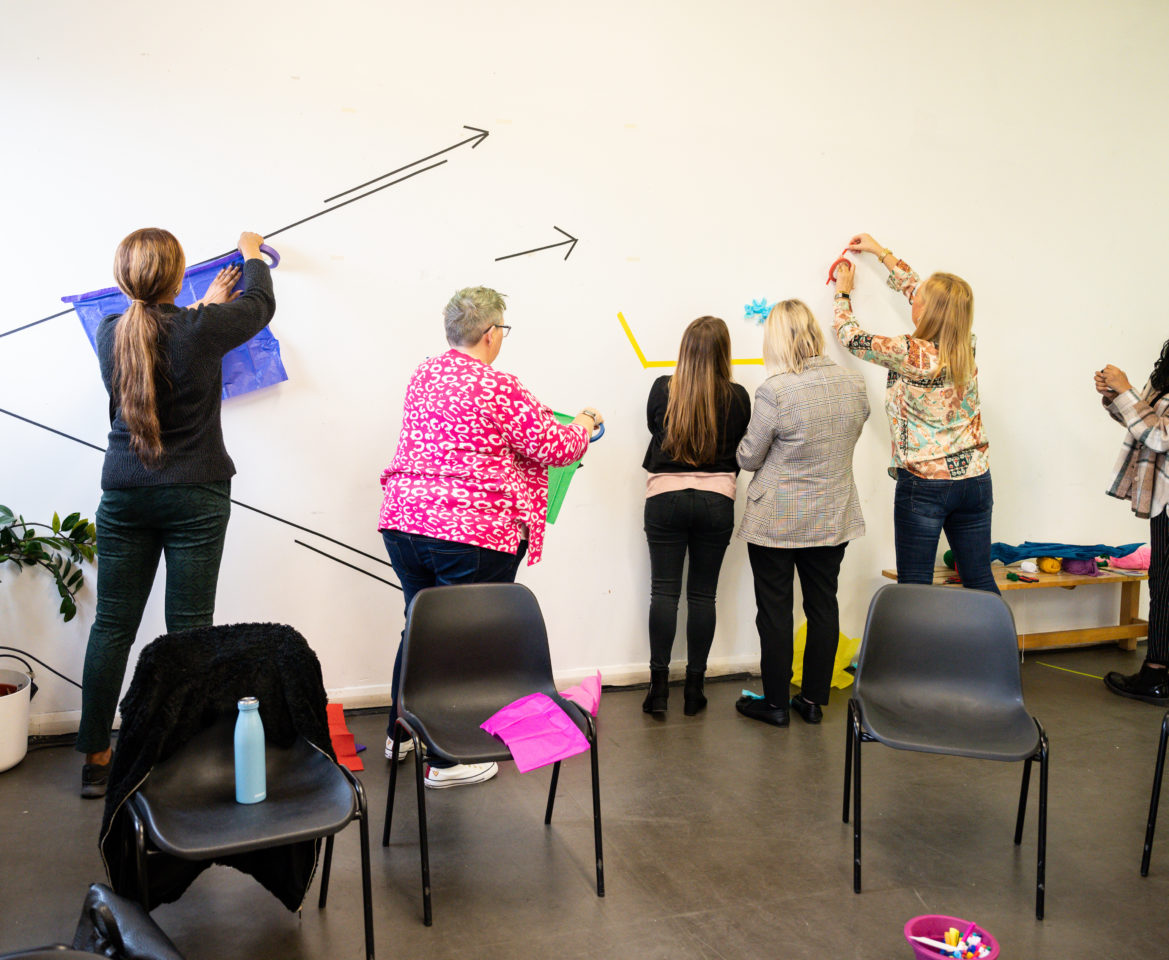 People in a room stick paper up in a wall as part of an activity.