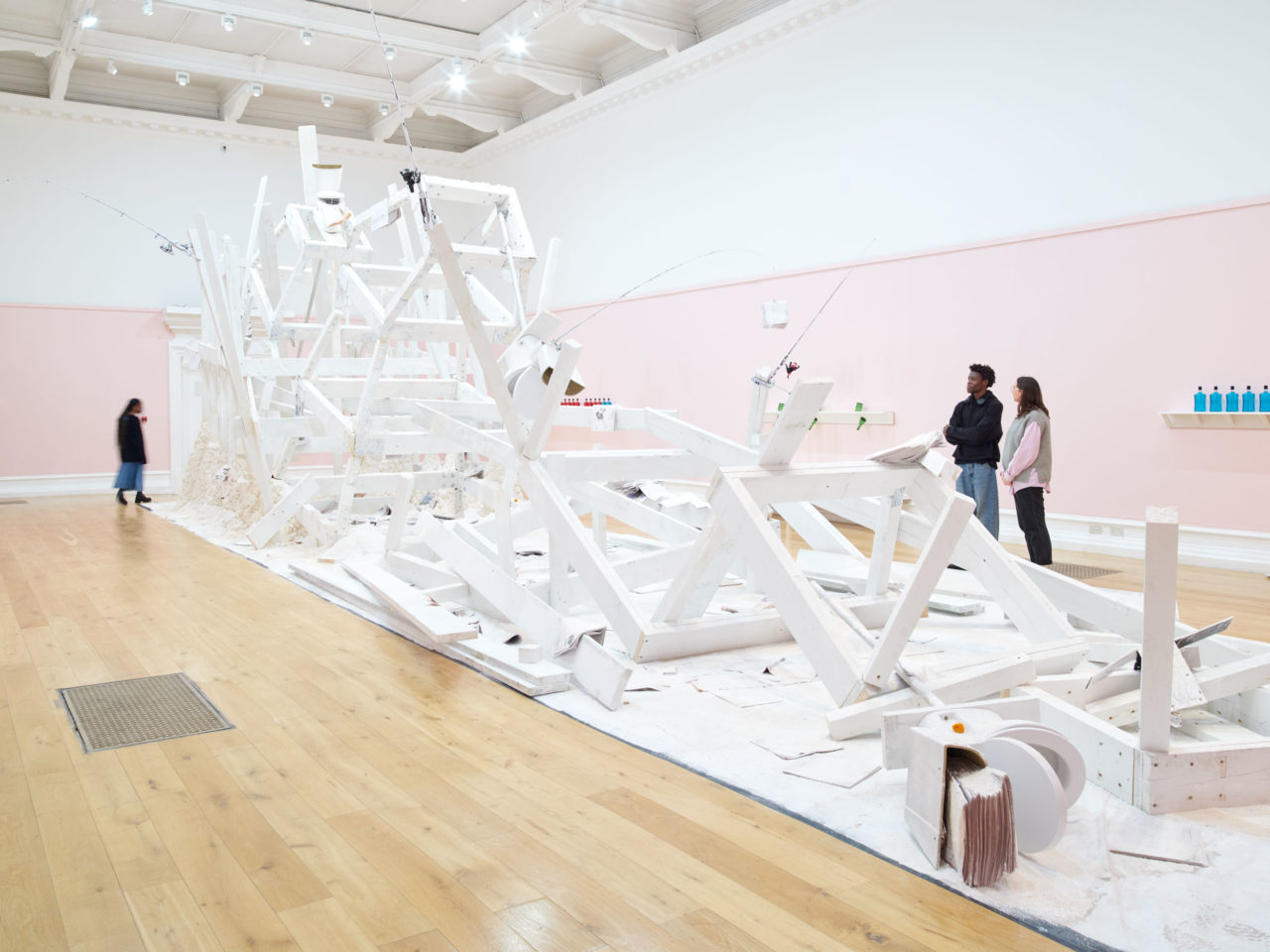 A wooden installation by artist Pope.L painted white and covered in flour in the centre of a large gallery with pink and white walls.