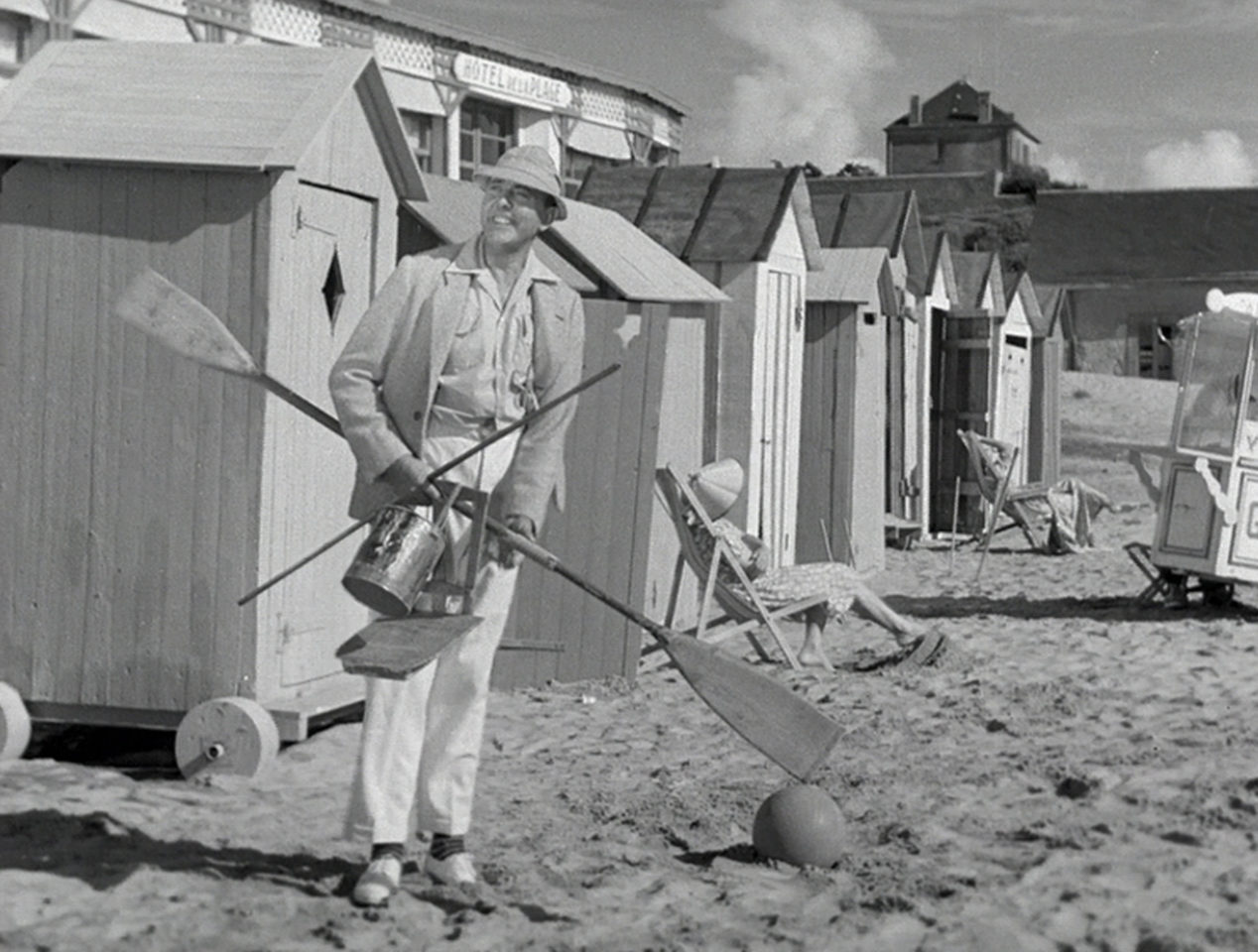 A man is standing on a beach holding two wooden oars.