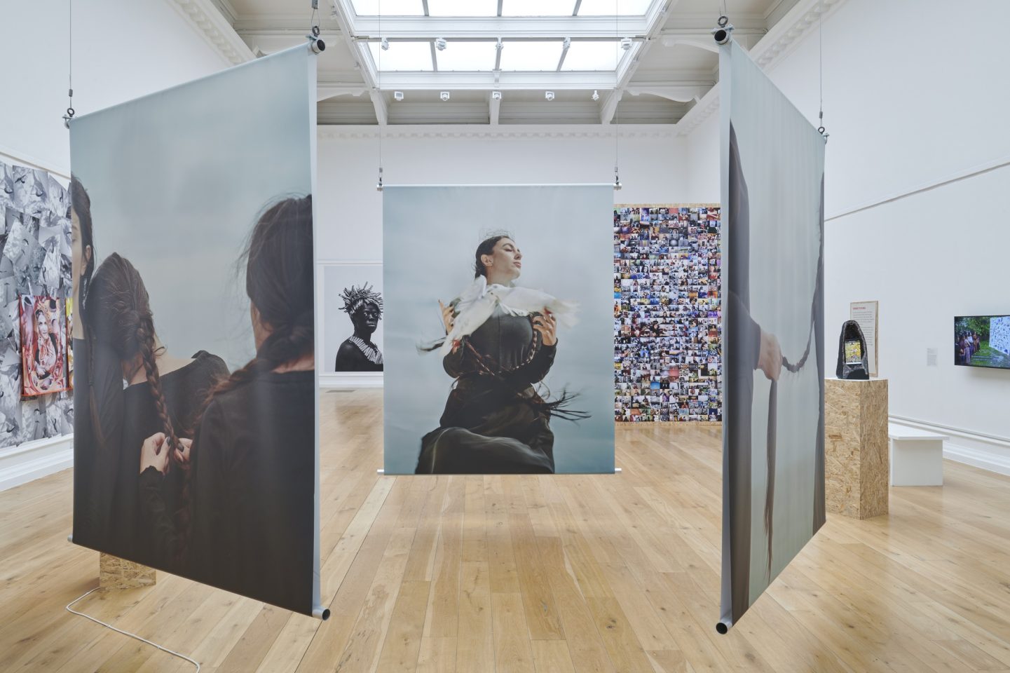 Hanging photographs in an art gallery. The work is by Hoda Afshar and features a woman holding a dove.