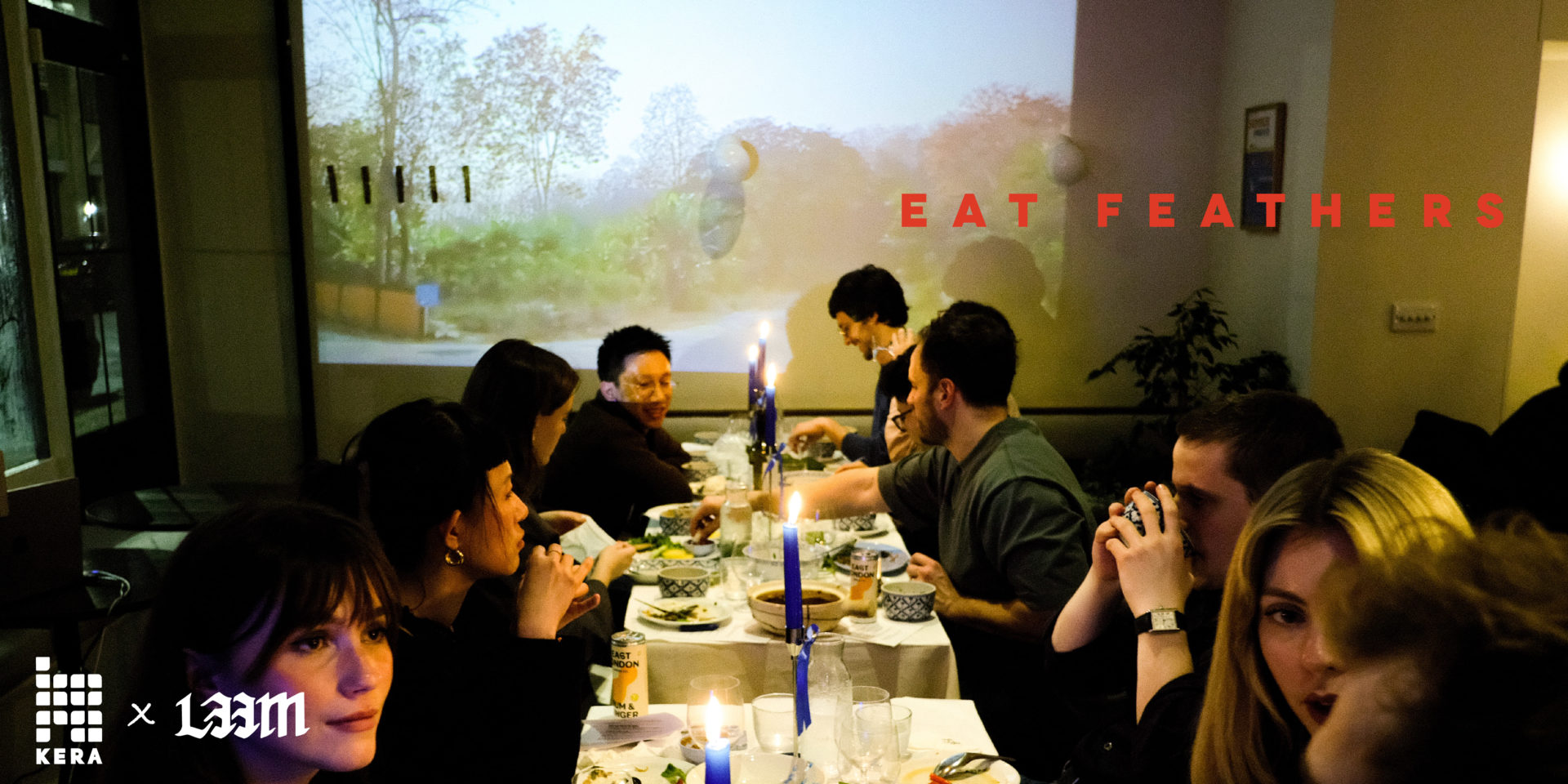 A group of people sit at a dinner table, talking, eating and drinking.
