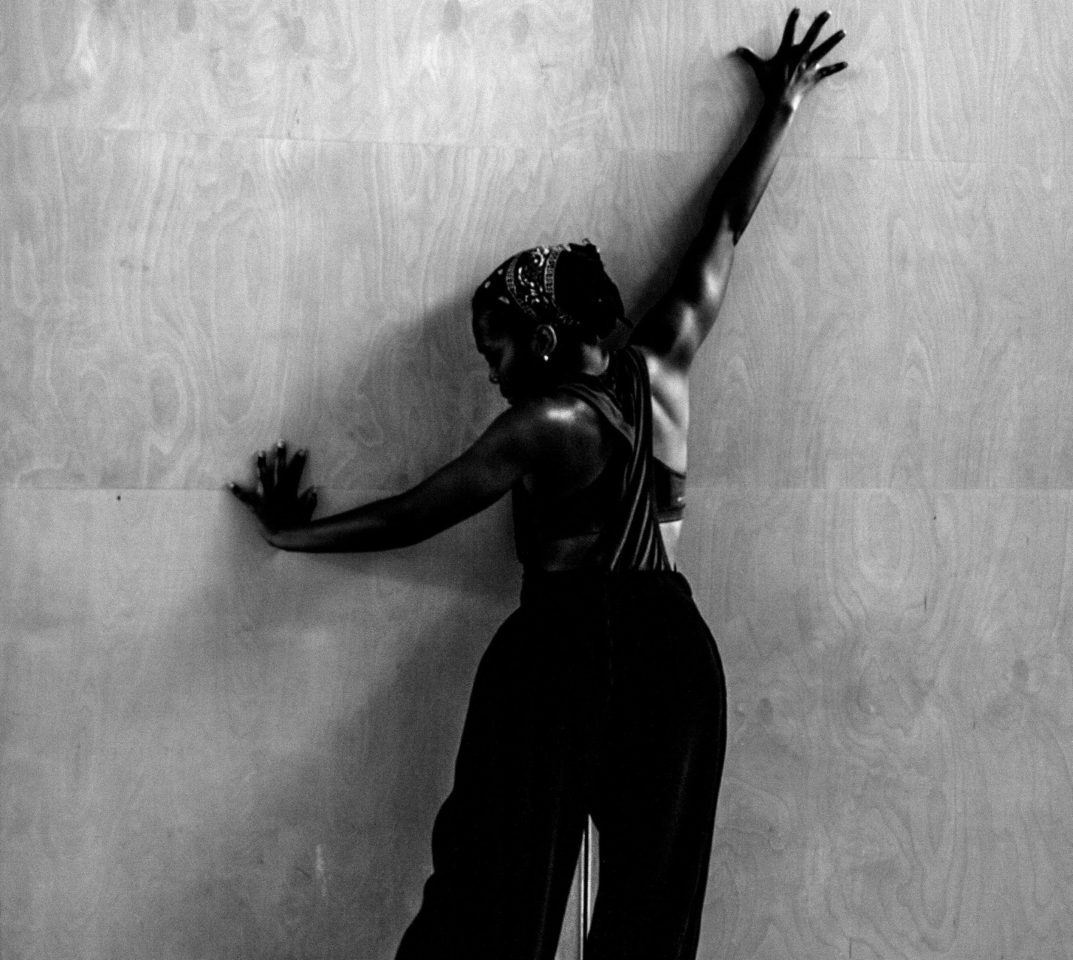 Dance artist Sia Gbamoi is facing a wall with arms stretched across it